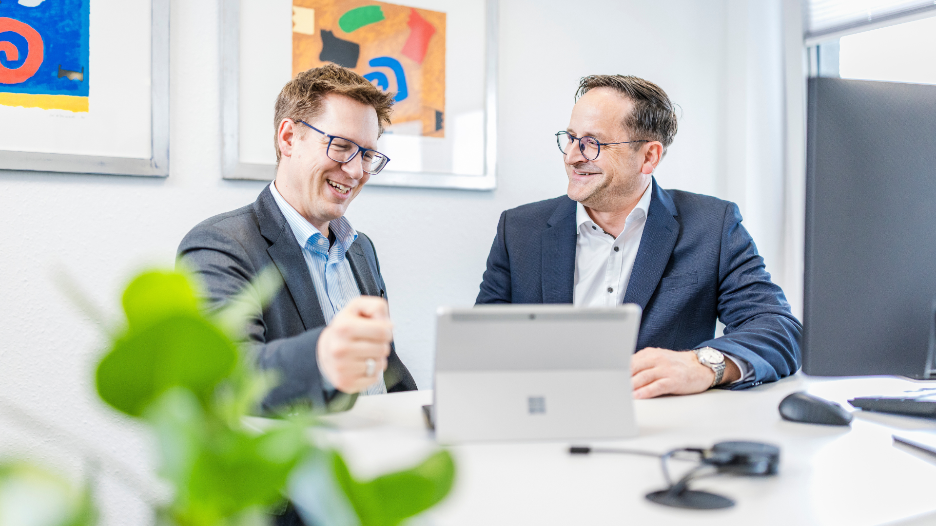 Daniel Faust zeigt Ralf Heinstein etwas auf dem Tablet. Sie lächeln dabei.